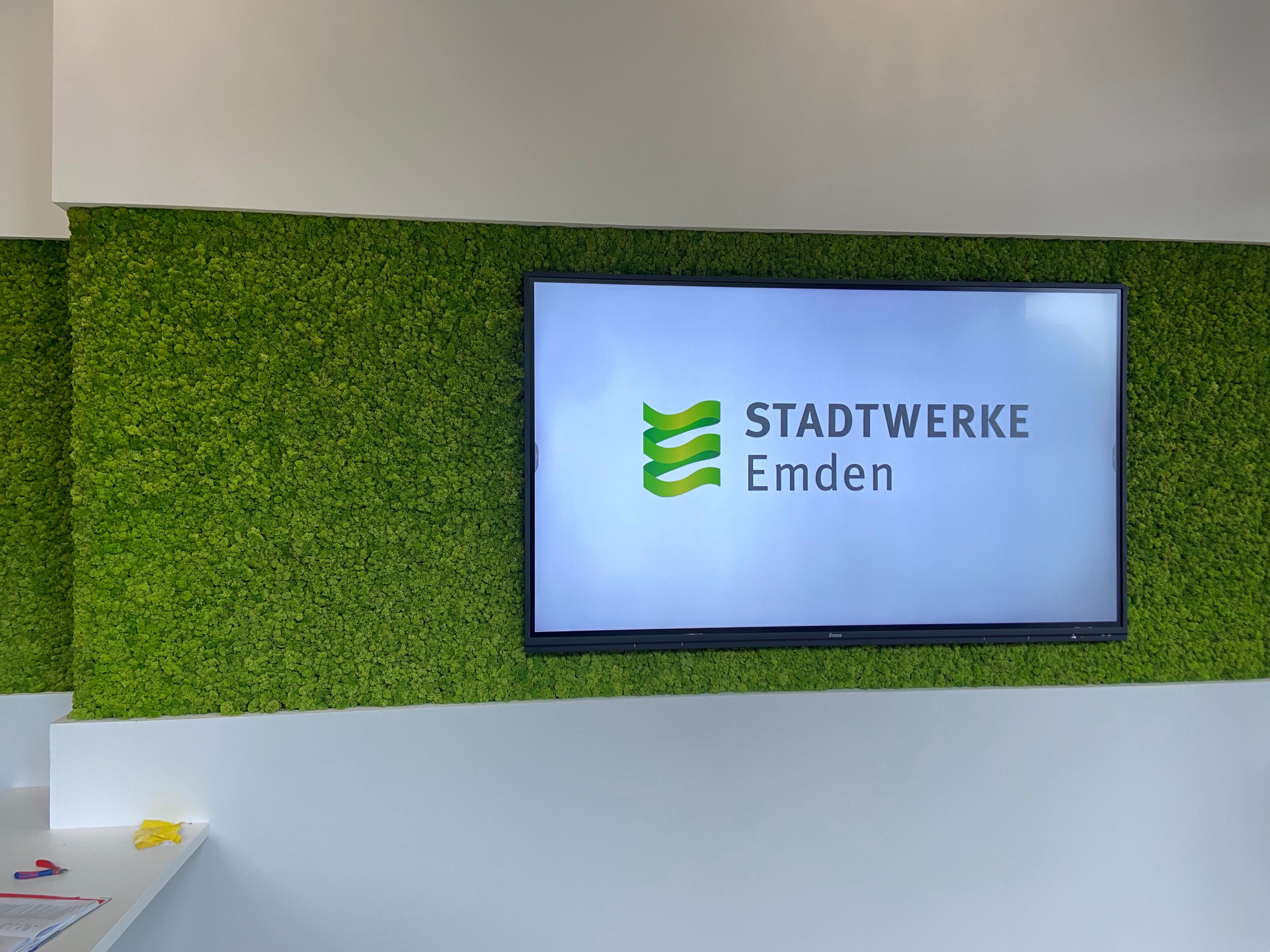 Großformatiges Display mit dem Logo der Stadtwerke Emden in einer grünen Mooswand