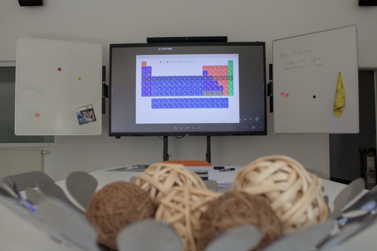 Modernes Klassenzimmer mit interaktivem Display, Lehrkraft startet die Präsentation per Knopfdruck