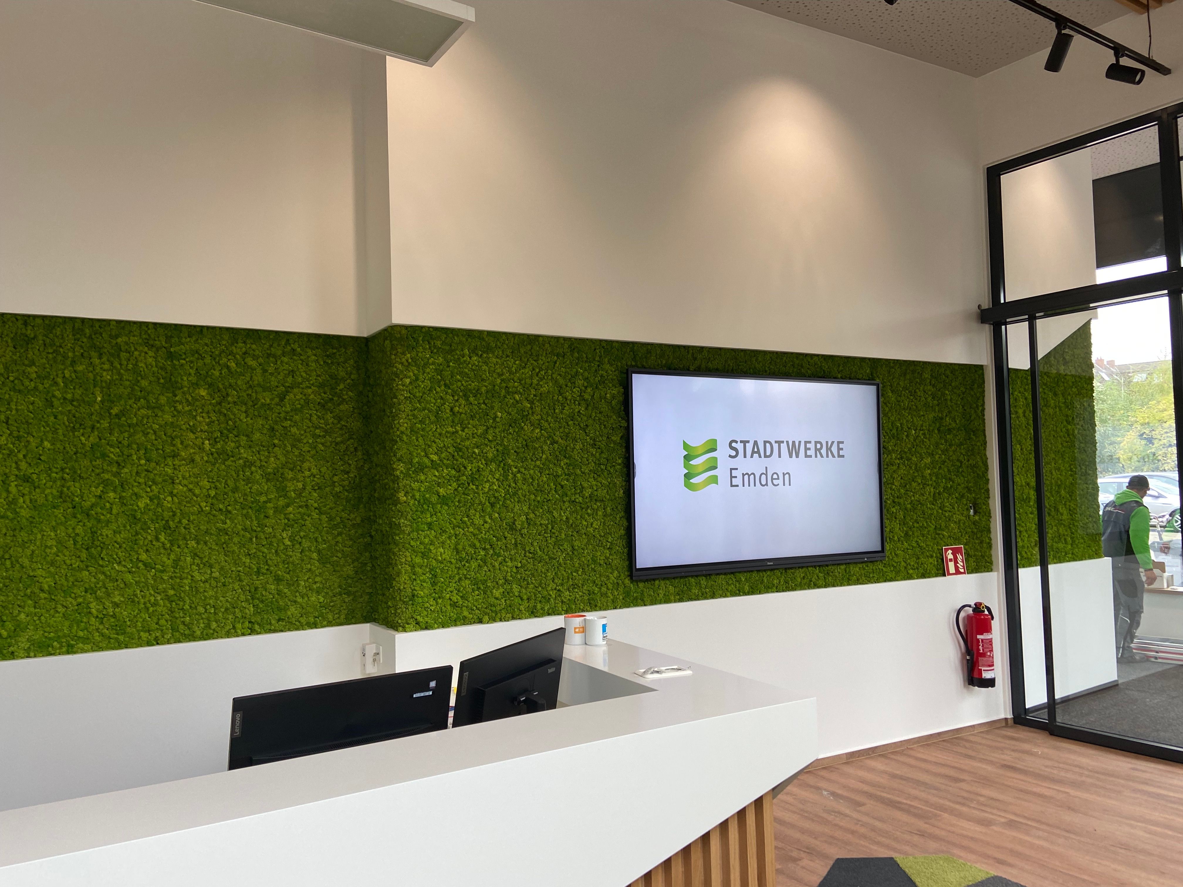 Empfangstresen im Kundencenter der Stadtwerke Emden, dahinter ein großformatiges Display mit Stadtwerke-Logo in der Mooswand