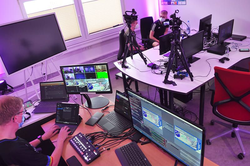 Regieplatz mit Videomischer-Bedienpult, Multiview-Monitor und Laptops, im Hintergrund Spielplätze mit zwei Camcordern auf Stativen