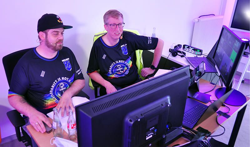 Zwei Moderatoren mit Headset-Mikrofonen im Trikot von Borussia Leer am Kommentatorenplatz