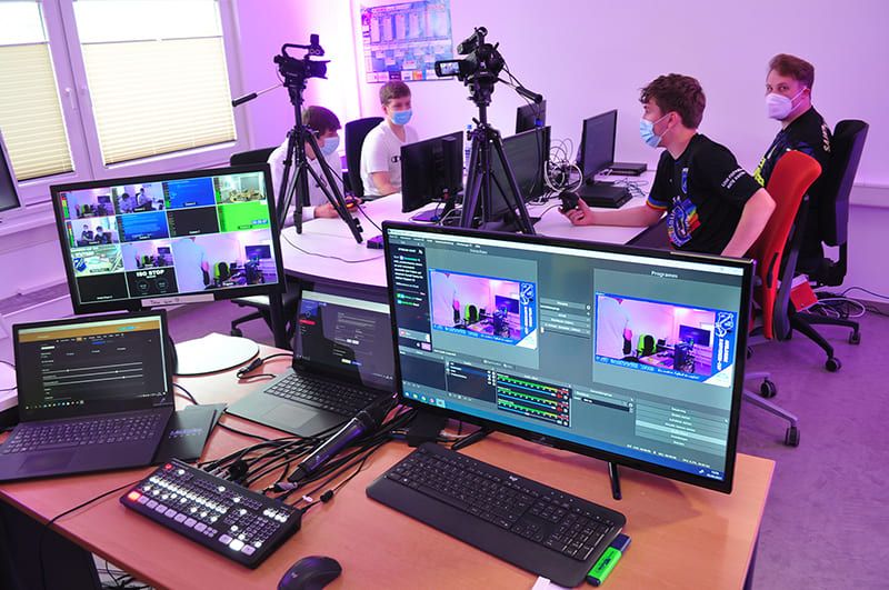 Regiebildschirm mit Vorschau- und Programmbild der Streaming-Software, dahinter Spieler und Kameras