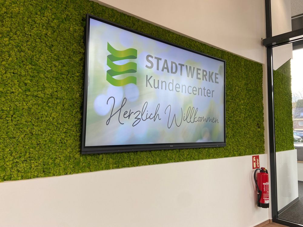 Wanddisplay in der Mooswand mit der Begrüßung „Stadtwerke Kundencenter – Herzlich Willkommen“