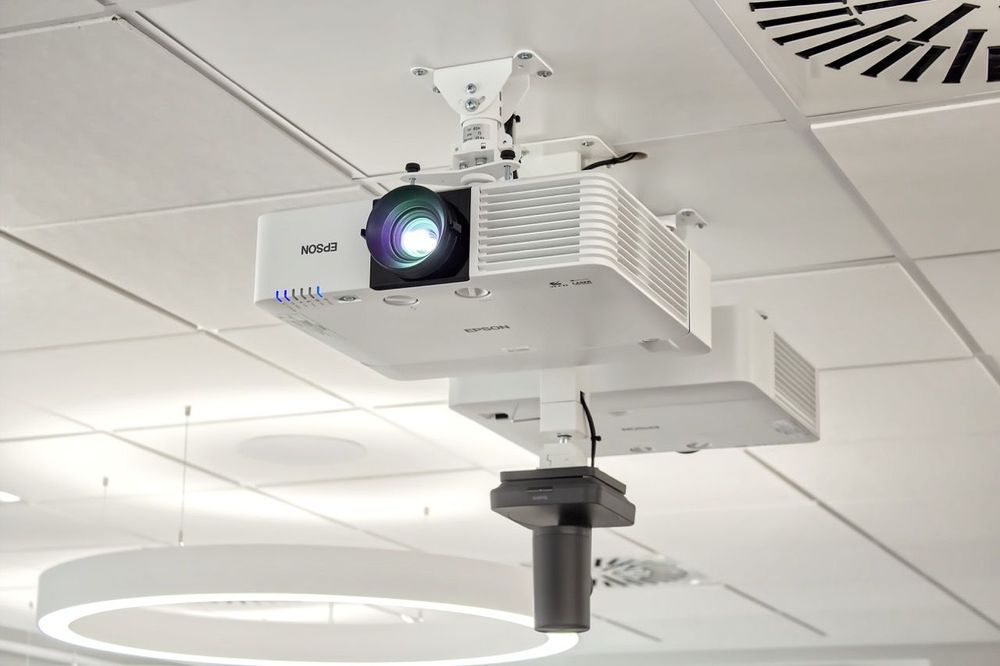 Epson-Laserprojektor an einer Deckenhalterung, dahinter der zweite Projektor und die PTZ-Kamera